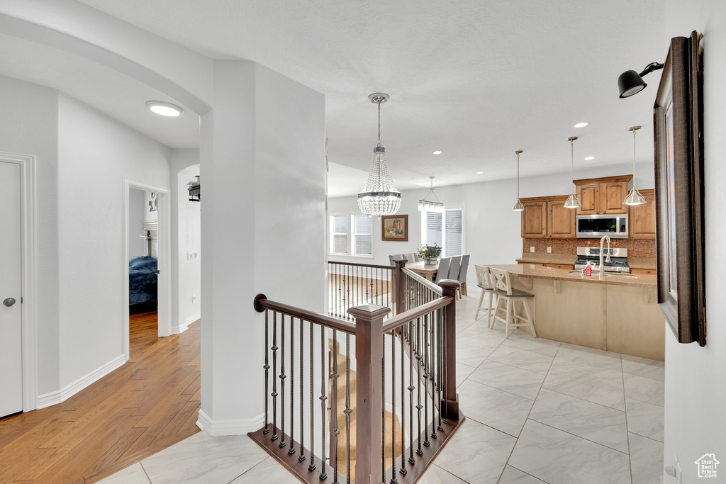 Hall featuring an upstairs landing, recessed lighting, baseboards, a sink, and arched walkways