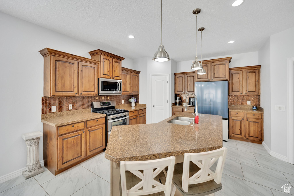 Kitchen featuring appliances with stainless steel finishes, a sink, baseboards, tasteful backsplash, and brown cabinets