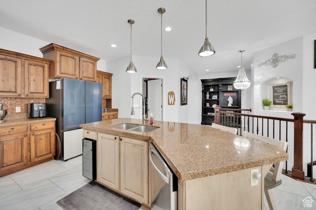 Kitchen featuring a sink, appliances with stainless steel finishes, backsplash, light stone countertops, and an island with sink