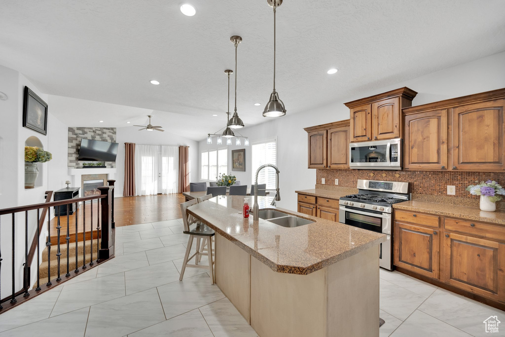 Kitchen with appliances with stainless steel finishes, a sink, ceiling fan, open floor plan, and an island with sink