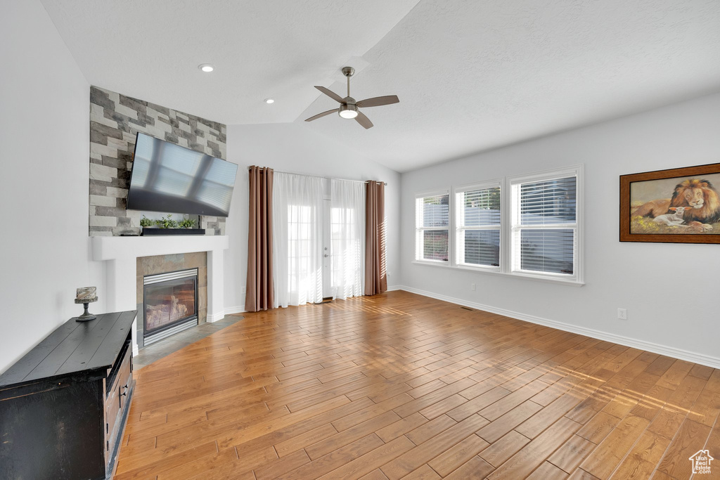 Unfurnished living room featuring a ceiling fan, light wood-type flooring, vaulted ceiling, a large fireplace, and baseboards