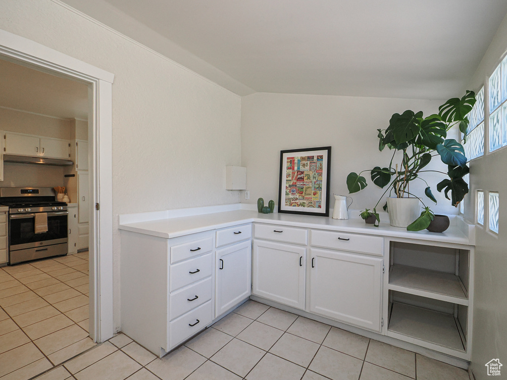 Kitchen with gas stove, light tile patterned floors, under cabinet range hood, white cabinets, and vaulted ceiling