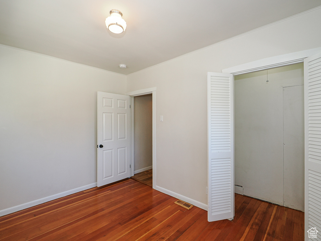 Unfurnished bedroom with hardwood / wood-style floors, a closet, baseboards, and ornamental molding