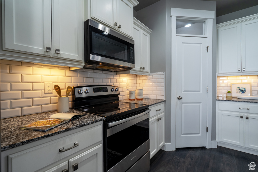Kitchen featuring appliances with stainless steel finishes, backsplash, dark stone counters, white cabinetry, and dark wood-style floors