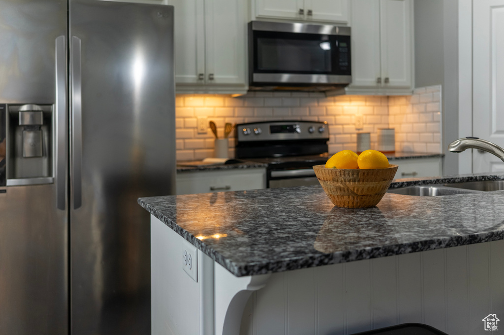 Kitchen with stainless steel appliances, a sink, dark stone countertops, and backsplash