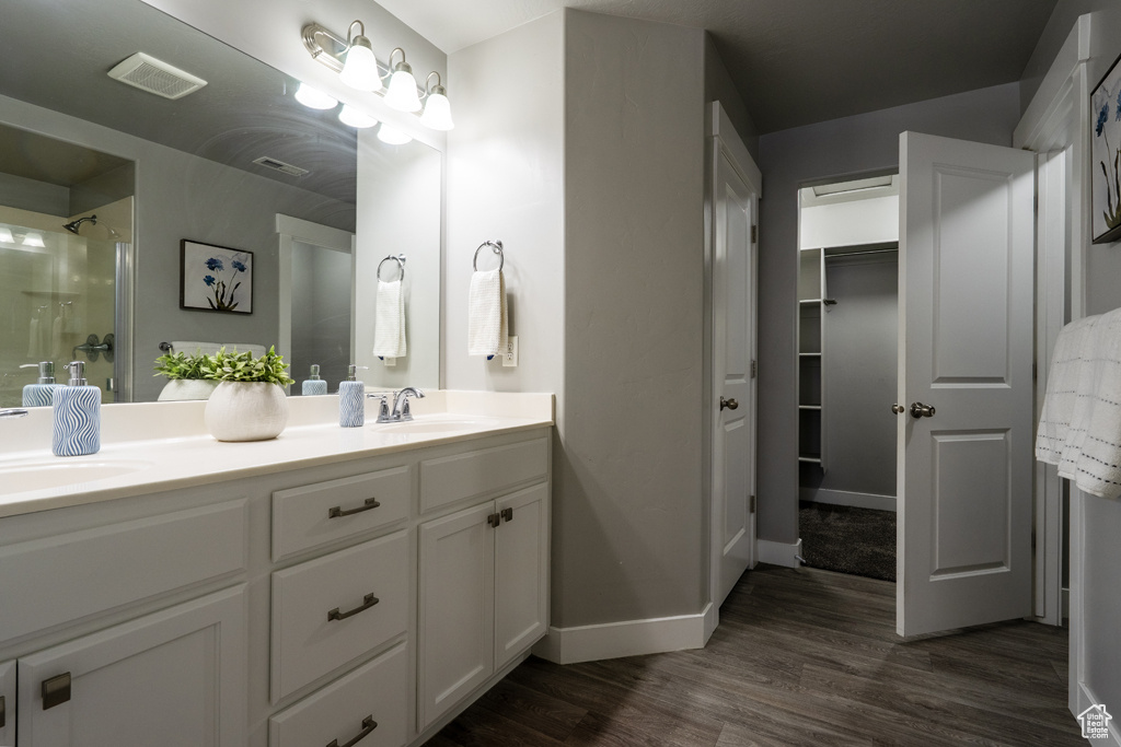 Bathroom featuring double vanity, wood finished floors, an enclosed shower, baseboards, and a walk in closet
