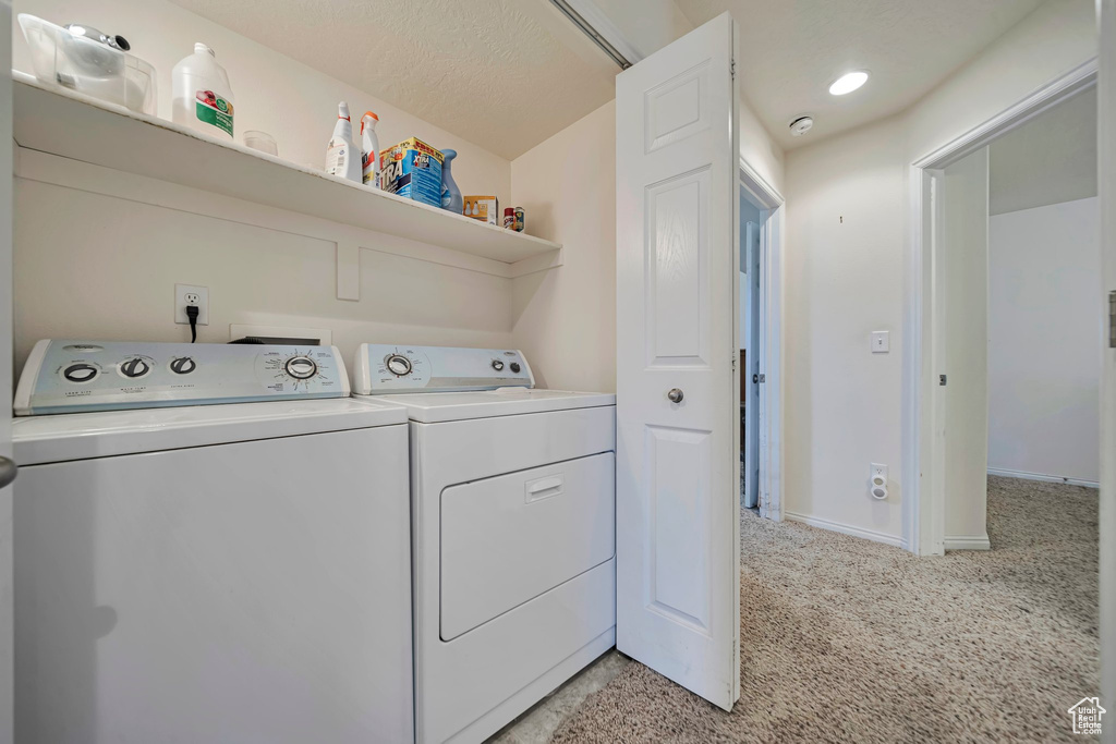 Laundry area featuring washing machine and dryer, light colored carpet, and baseboards