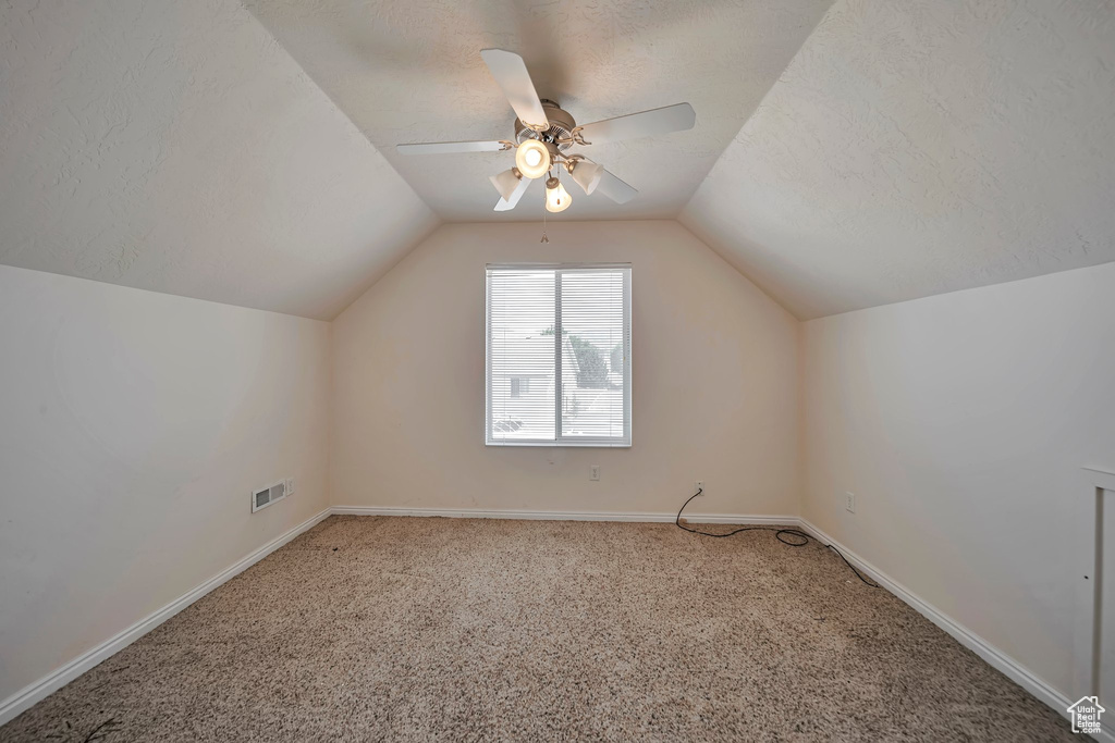 Additional living space featuring vaulted ceiling, carpet floors, a ceiling fan, baseboards, and a textured ceiling