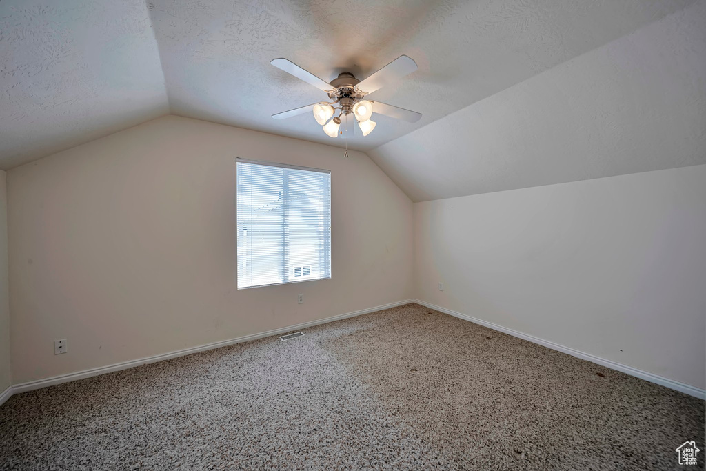 Additional living space with vaulted ceiling, a ceiling fan, a textured ceiling, carpet flooring, and baseboards
