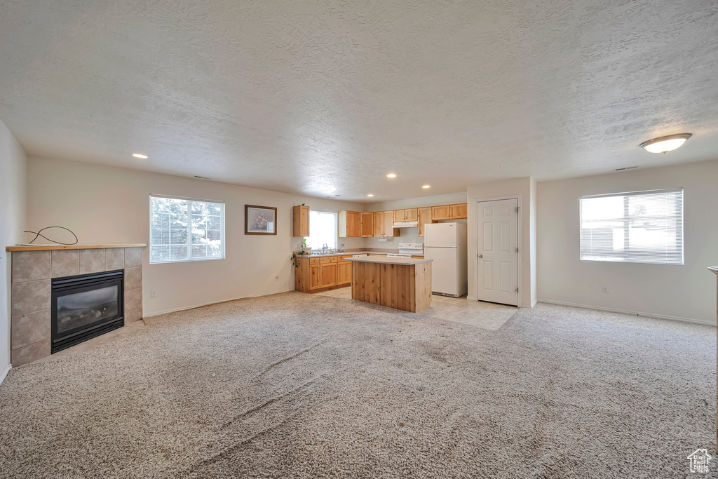 Unfurnished living room featuring recessed lighting, a tiled fireplace, light carpet, a textured ceiling, and baseboards