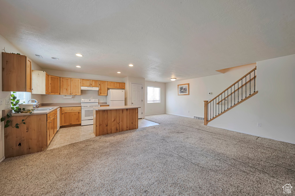 Kitchen featuring white appliances, a kitchen island, a sink, recessed lighting, and light colored carpet