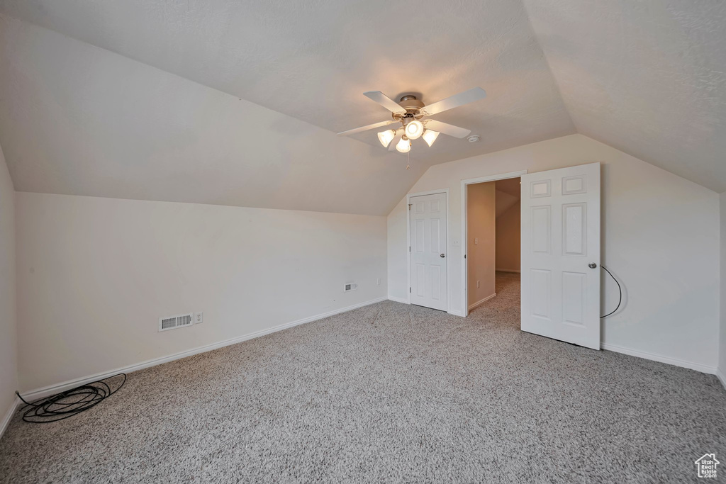 Additional living space featuring light colored carpet, vaulted ceiling, baseboards, and ceiling fan