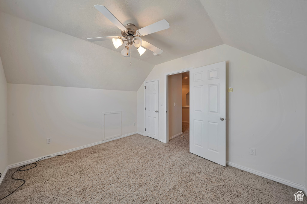 Additional living space featuring light colored carpet, lofted ceiling, a ceiling fan, and baseboards