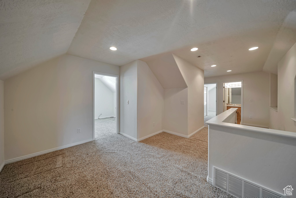 Additional living space featuring recessed lighting, light colored carpet, vaulted ceiling, baseboards, and a textured ceiling