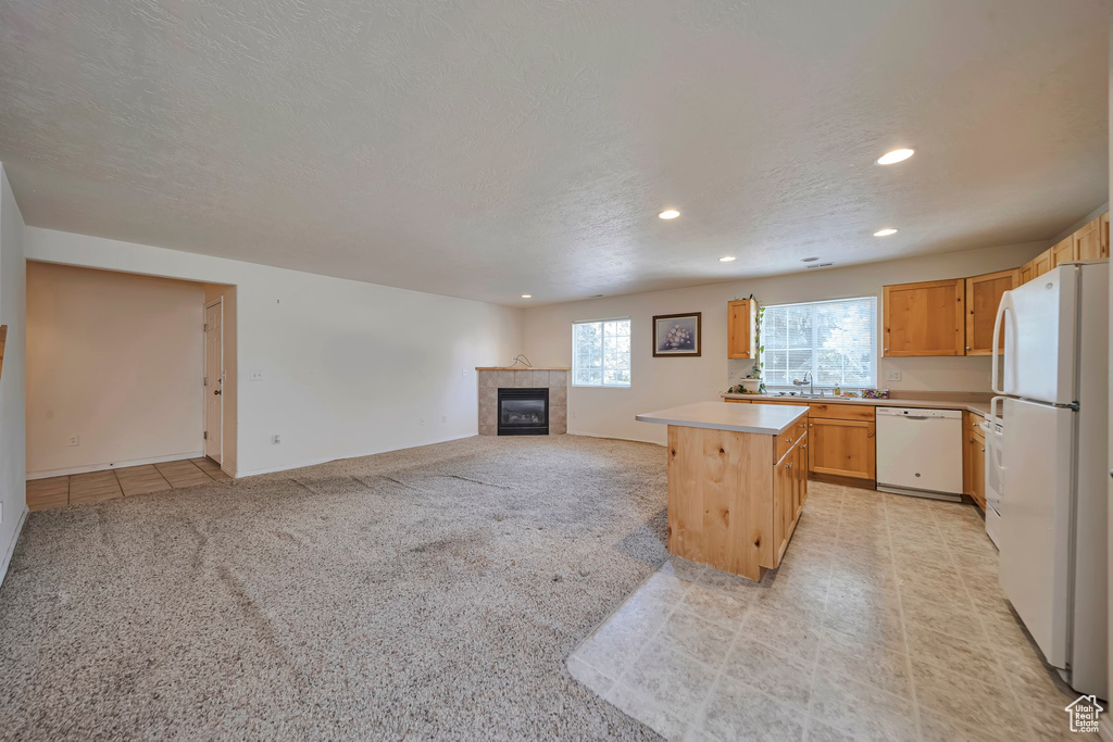 Kitchen with white appliances, recessed lighting, light countertops, a fireplace, and light carpet