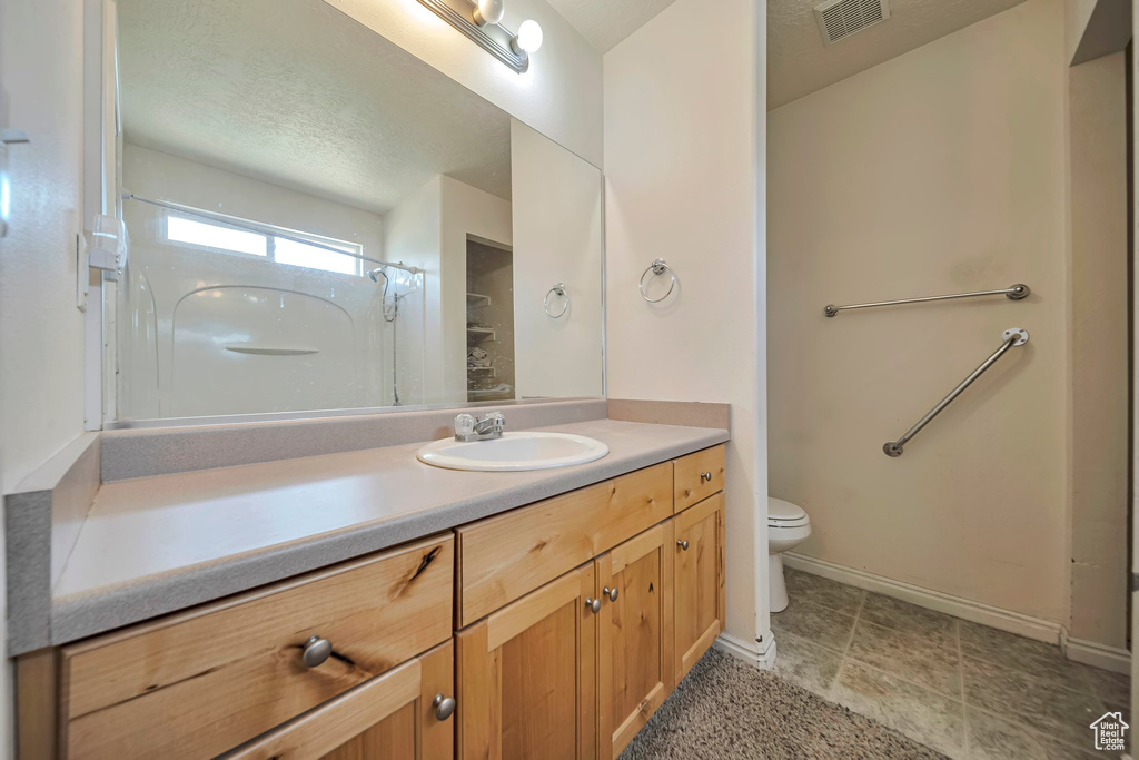 Bathroom with toilet, vanity, a shower, and baseboards