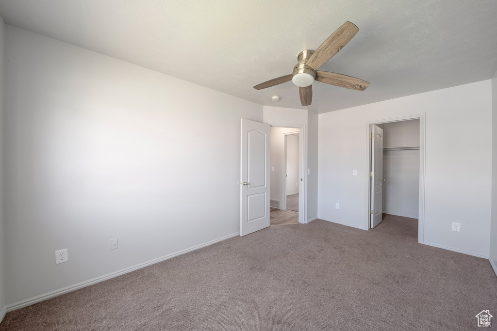 Unfurnished bedroom with light carpet, ceiling fan, a walk in closet, and baseboards