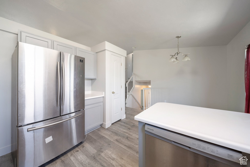 Kitchen with appliances with stainless steel finishes, light wood-style flooring, a chandelier, light countertops, and hanging light fixtures