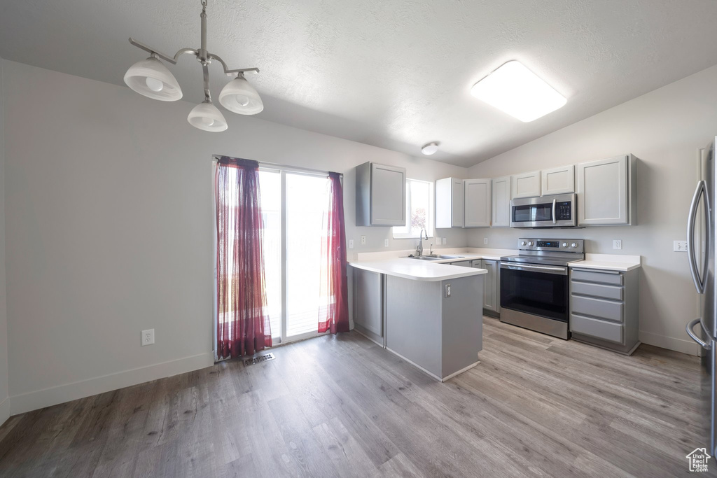 Kitchen featuring stainless steel appliances, a peninsula, light countertops, a sink, and gray cabinets
