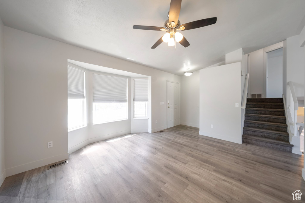 Unfurnished living room featuring a ceiling fan, stairs, light wood-style flooring, baseboards, and lofted ceiling