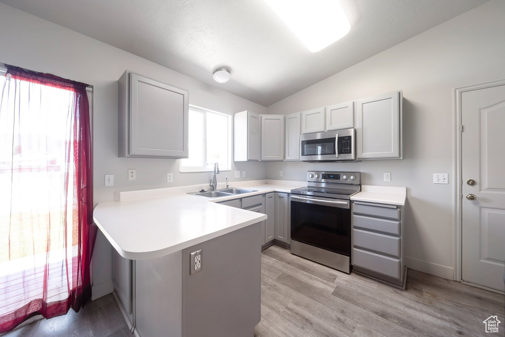 Kitchen with appliances with stainless steel finishes, a sink, gray cabinets, a peninsula, and vaulted ceiling
