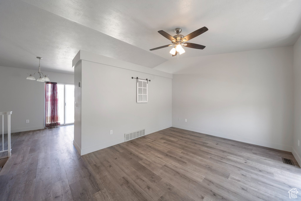 Empty room with ceiling fan, a chandelier, wood finished floors, and baseboards