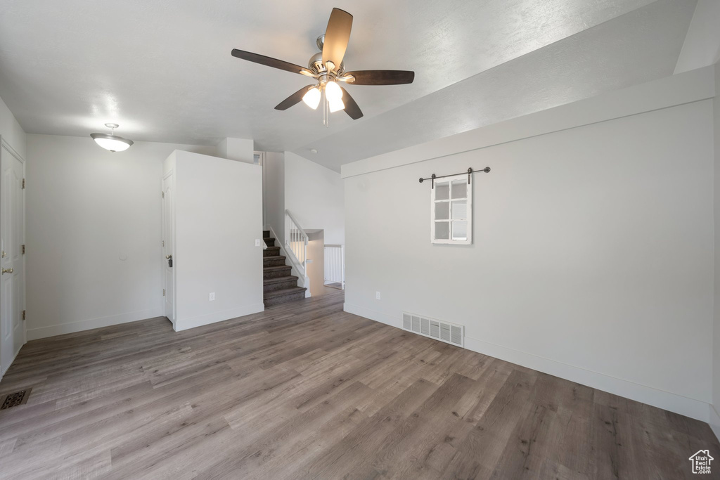 Spare room featuring a ceiling fan, stairway, wood finished floors, baseboards, and vaulted ceiling