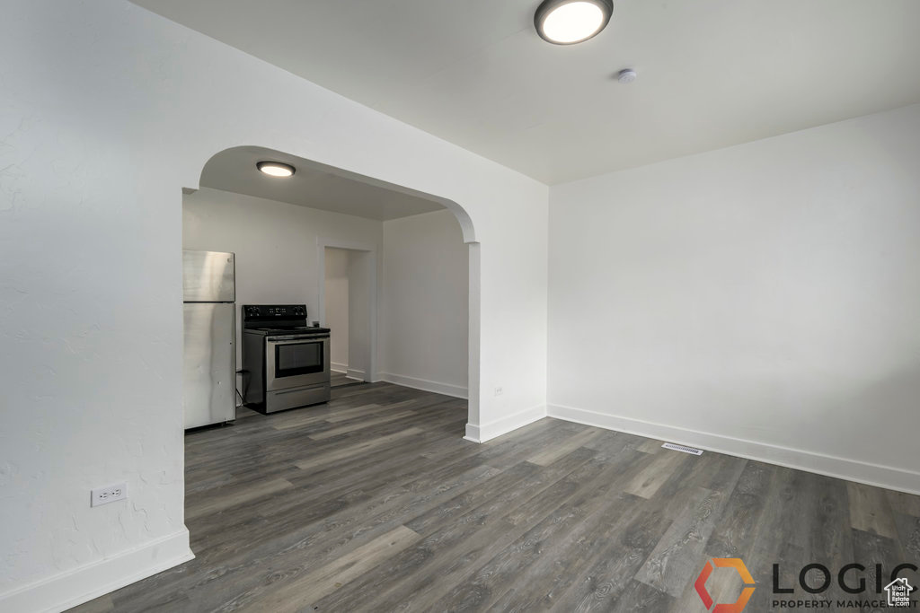 Unfurnished living room with arched walkways, baseboards, and dark wood-type flooring