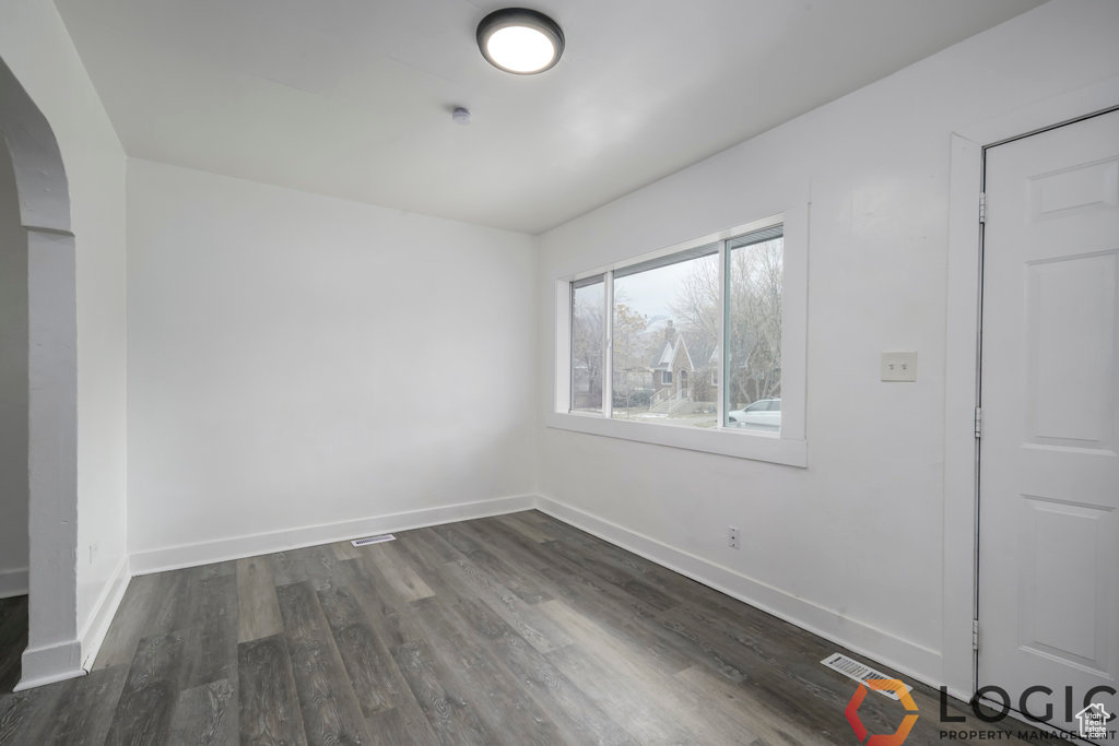 Spare room featuring arched walkways, dark wood-type flooring, and baseboards