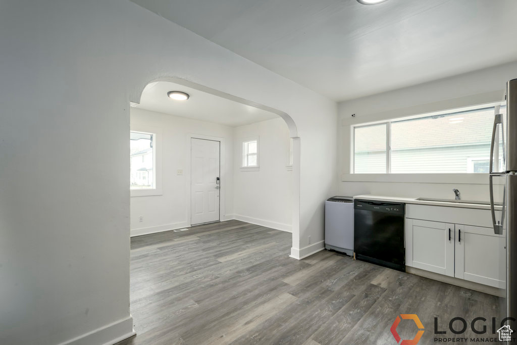 Kitchen with black dishwasher, arched walkways, dark wood-style floors, and baseboards