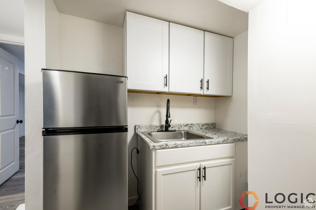 Kitchen featuring freestanding refrigerator, a sink, white cabinetry, wood finished floors, and light stone countertops