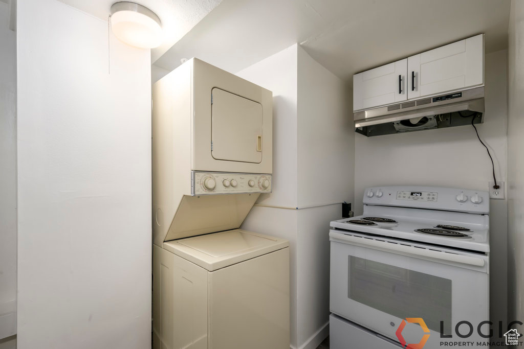 Kitchen with electric range, stacked washing machine and dryer, under cabinet range hood, white cabinets, and light countertops