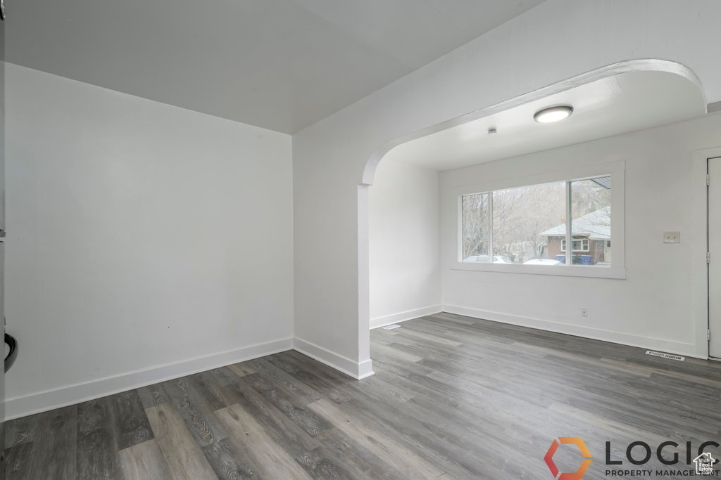 Empty room featuring arched walkways, dark wood finished floors, and baseboards