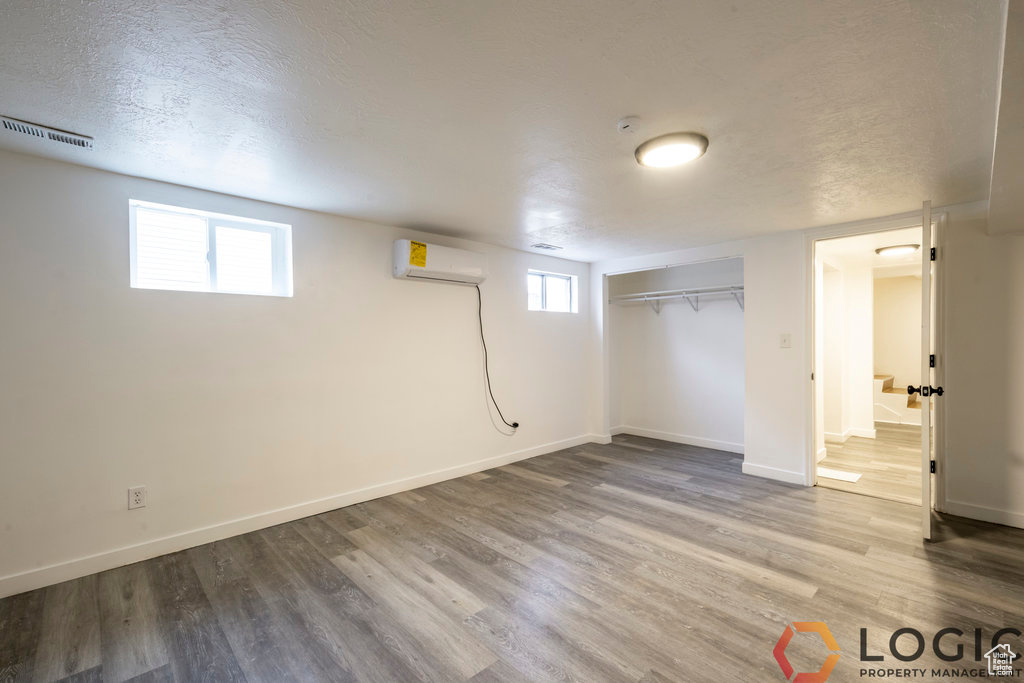 Below grade area featuring an AC wall unit, wood finished floors, baseboards, and a textured ceiling