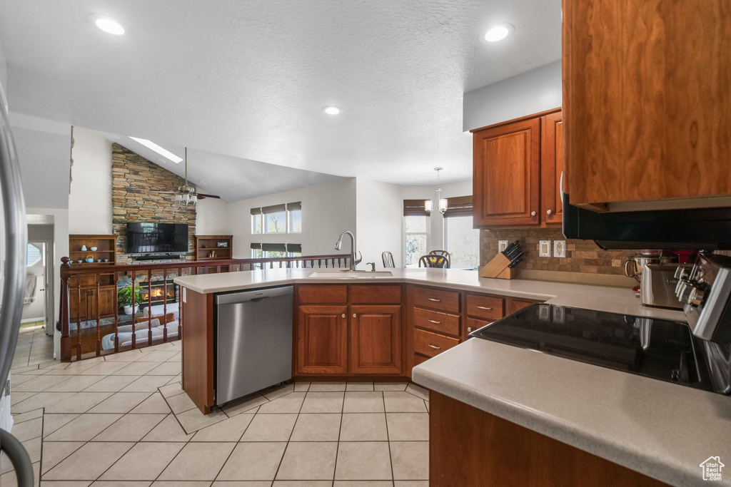 Kitchen with appliances with stainless steel finishes, a sink, a peninsula, brown cabinetry, and light countertops