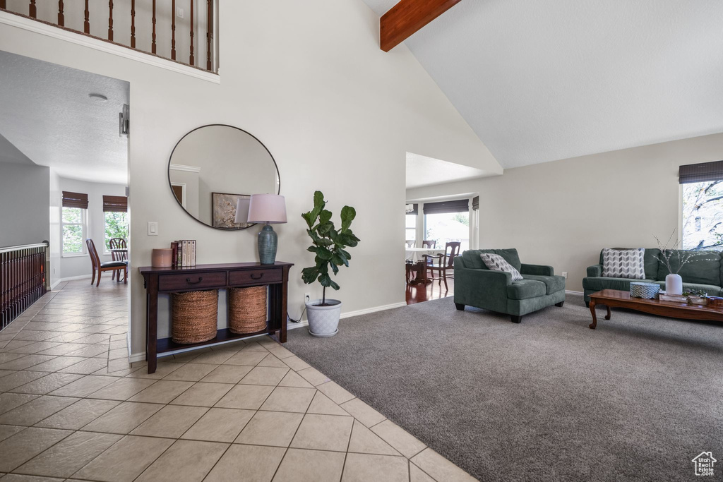 Living area featuring high vaulted ceiling, beamed ceiling, light tile patterned flooring, baseboards, and light colored carpet