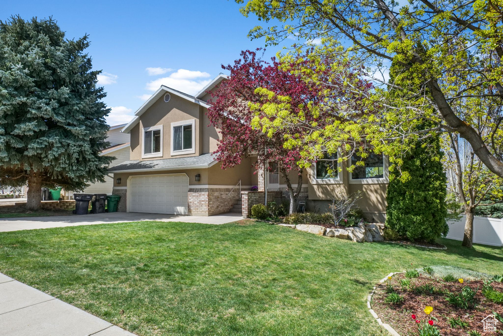 View of property hidden behind natural elements featuring an attached garage, stucco siding, brick siding, driveway, and a front lawn