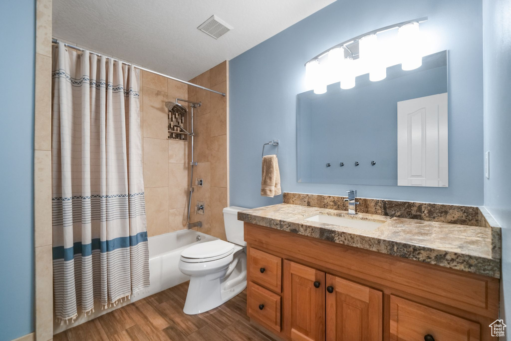 Full bath featuring wood finished floors, vanity, shower / bathtub combination with curtain, and toilet