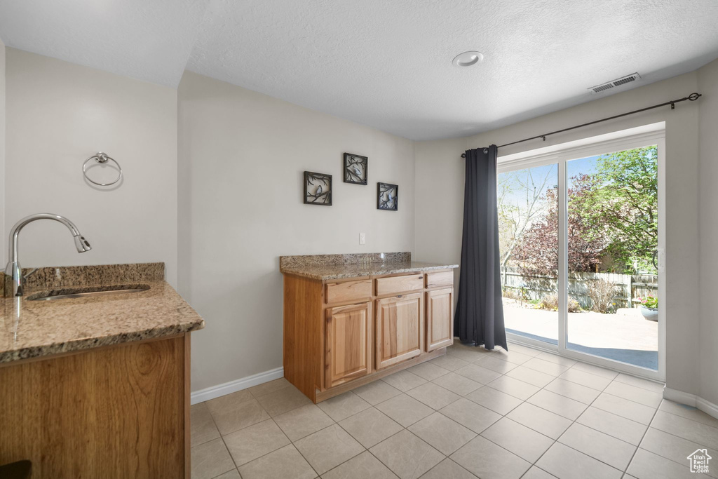 Kitchen featuring a sink, light stone counters, a textured ceiling, baseboards, and light tile patterned floors