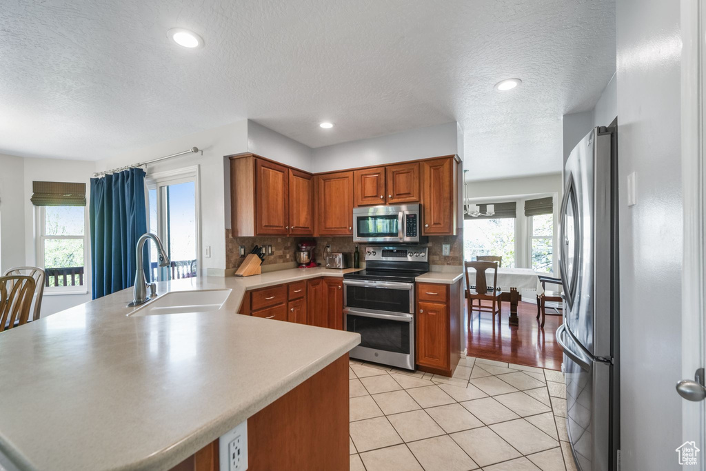 Kitchen featuring stainless steel appliances, a sink, a peninsula, a textured ceiling, and brown cabinetry