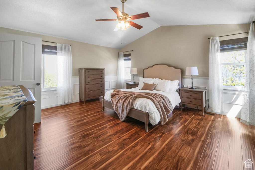 Bedroom with wood finished floors, a wainscoted wall, vaulted ceiling, and multiple windows