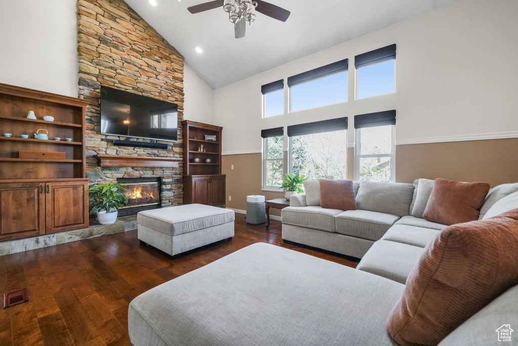 Living room featuring high vaulted ceiling, ceiling fan, a fireplace, dark wood-style flooring, and baseboards