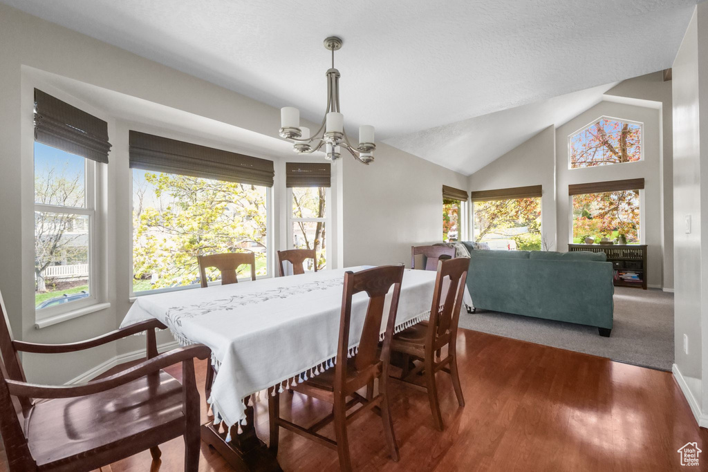 Dining space with a chandelier, plenty of natural light, wood finished floors, baseboards, and lofted ceiling