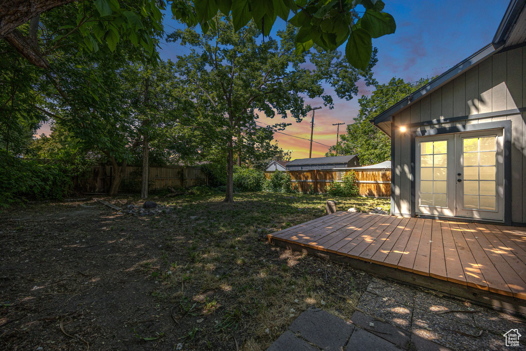 Yard at dusk with french doors, a fenced backyard, and a deck