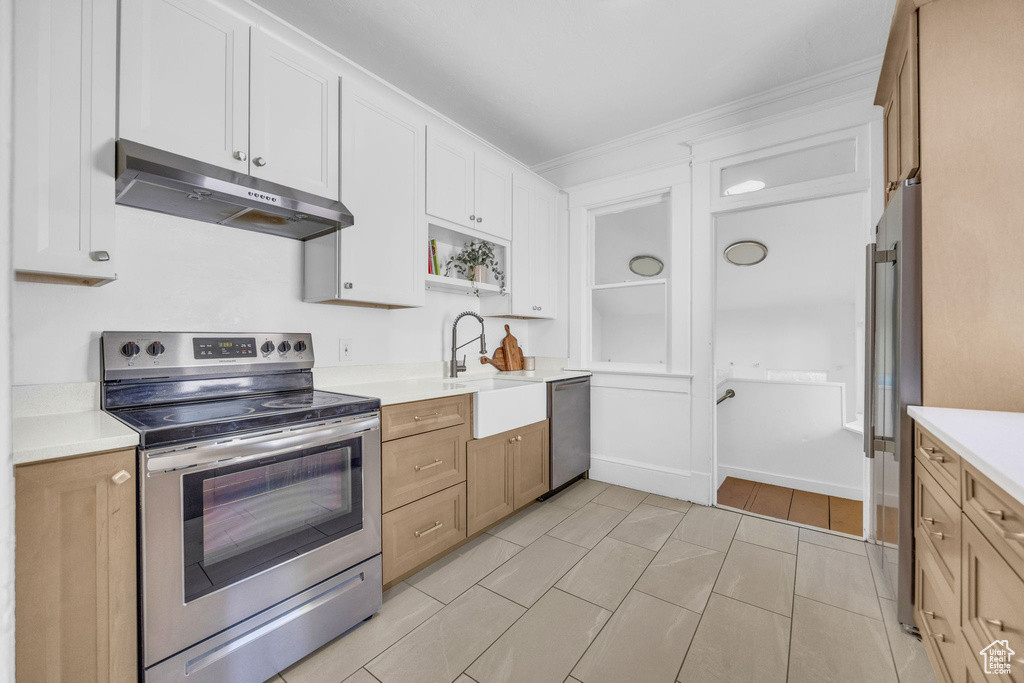 Kitchen featuring stainless steel appliances, under cabinet range hood, a sink, light countertops, and crown molding