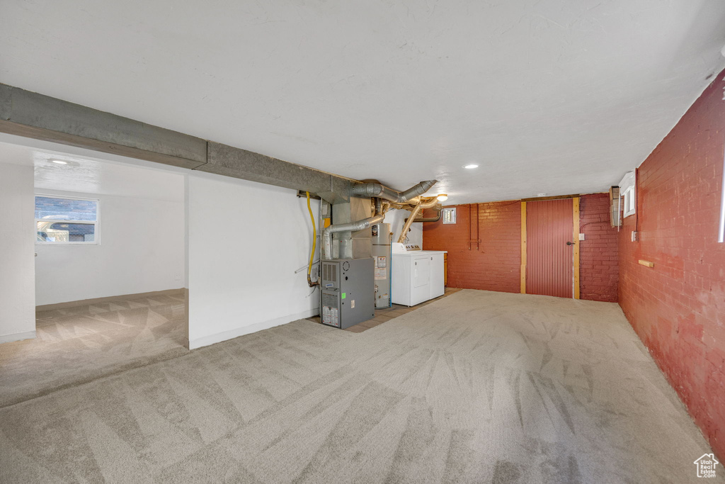 Below grade area featuring carpet floors, brick wall, heating unit, baseboards, and washing machine and clothes dryer
