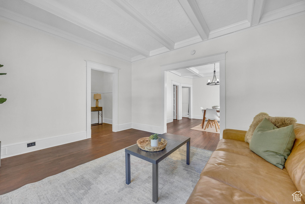 Living area featuring beam ceiling, wood finished floors, a chandelier, crown molding, and baseboards