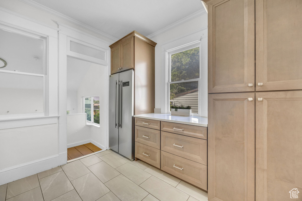Kitchen featuring high end fridge, healthy amount of natural light, light countertops, ornamental molding, and light tile patterned floors