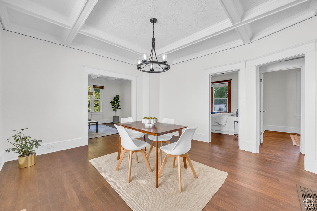 Dining area with coffered ceiling, healthy amount of natural light, a chandelier, dark wood-style floors, and beamed ceiling