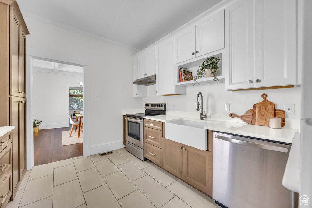 Kitchen with stainless steel appliances, a sink, under cabinet range hood, crown molding, and light countertops